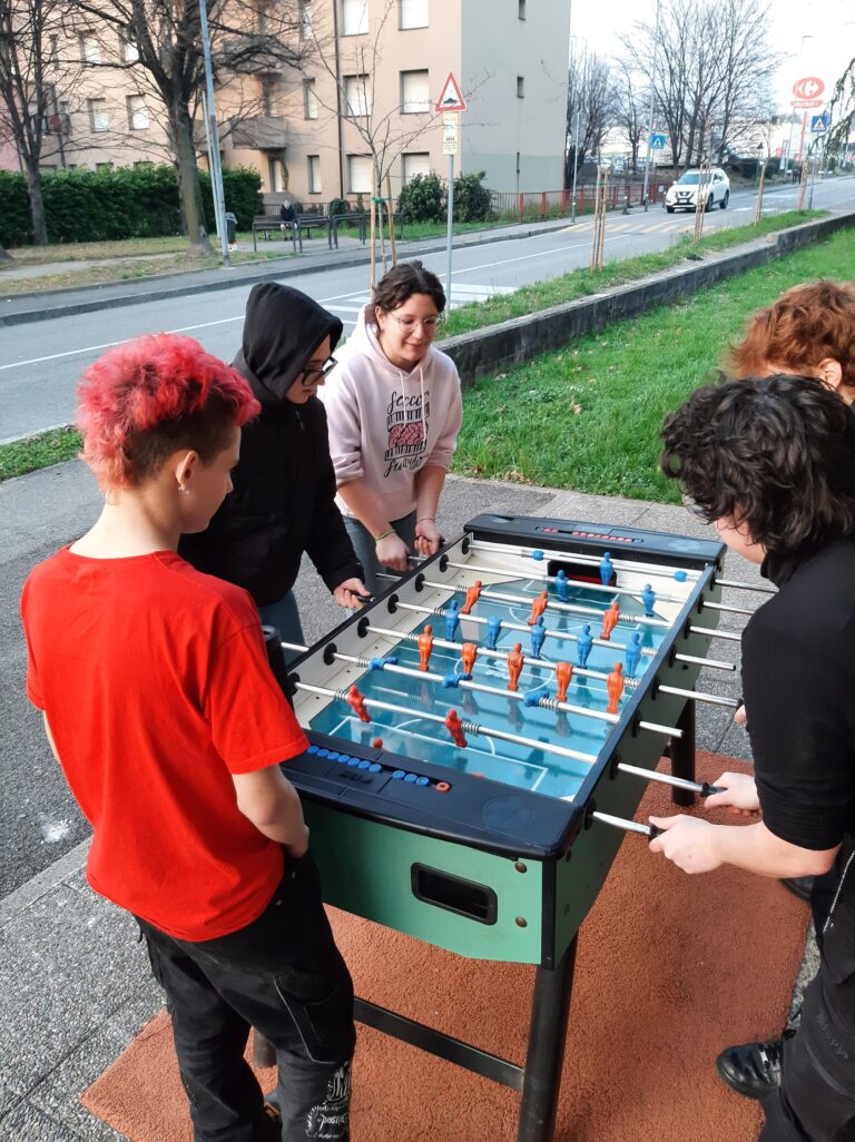 Un gruppo di giovani gioca a calcio balilla in uno spazio esterno.
