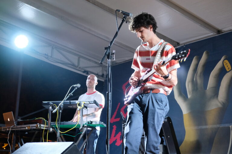 Due ragazzi stanno suonando su un palco. Uno di loro è alla tastiera, l'altro alla chitarra.