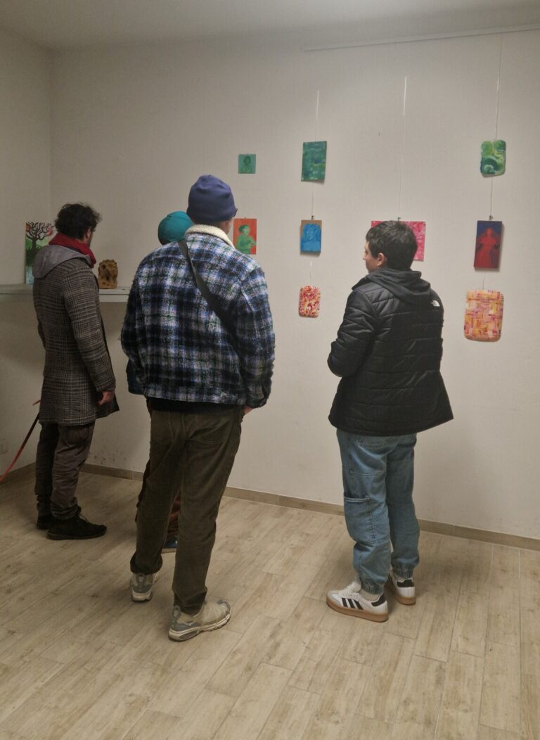 Quattro persone stanno visitando una mostra artistica, osservando dei quadri appesi alle pareti. Alcuni sono ritratti, altri composizioni astratte.