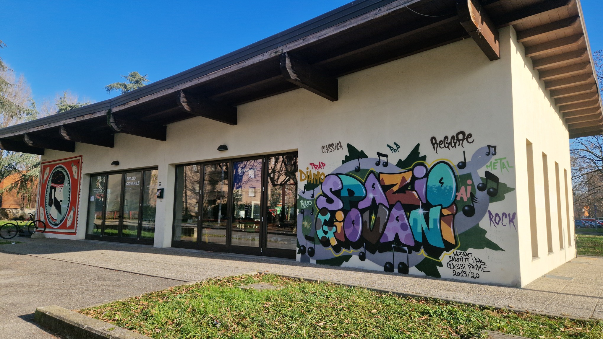 La facciata esterna dello Spazio per Giovani a Boccaleone. Ha pareti chiare ravvivate da due murales colorati e grandi vetrate