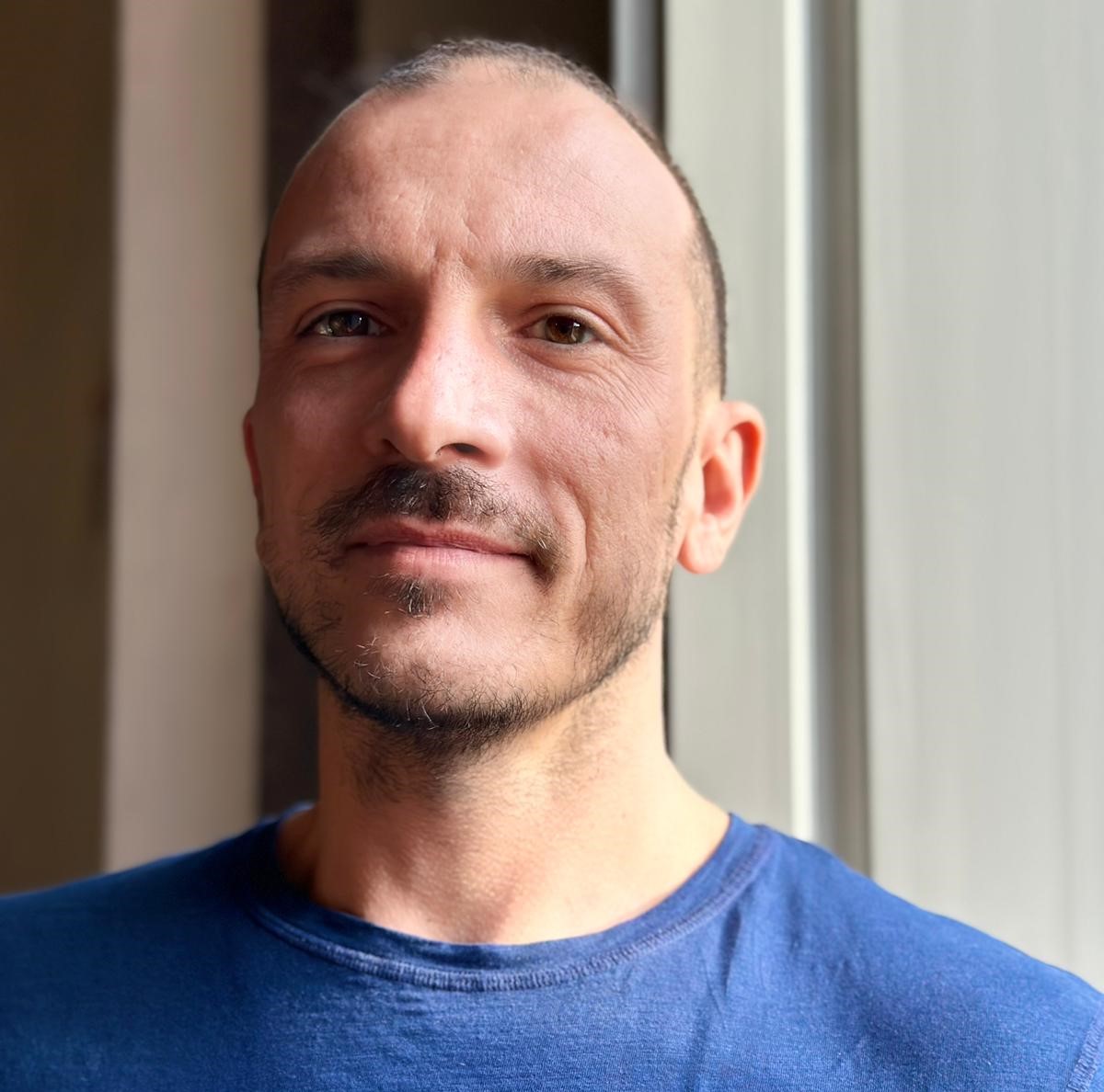 Primo piano di Diego accanto a una finestra. Ha una felpa blu.