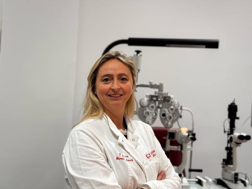 Monica in questa foto ha le braccia incrociate e sorride. H aun camice bianco e dietro di lei si vedono delle strumentazioni di laboratorio.