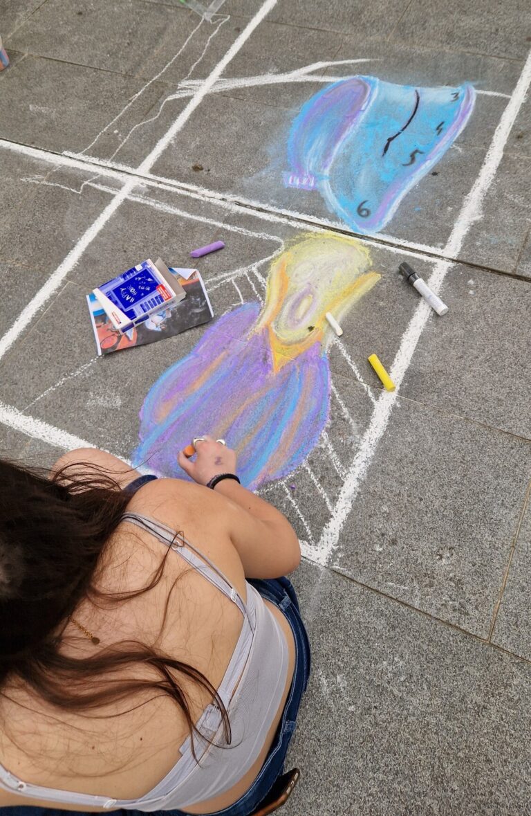 Una ragazza, fotografata dall'alto, sta disegnando con dei gessetti su una pavimentazione esterna. Il soggetto è l'urlo di Munch. Poco più in alto ha disegnato l'orologio che si scioglie di Dalì.