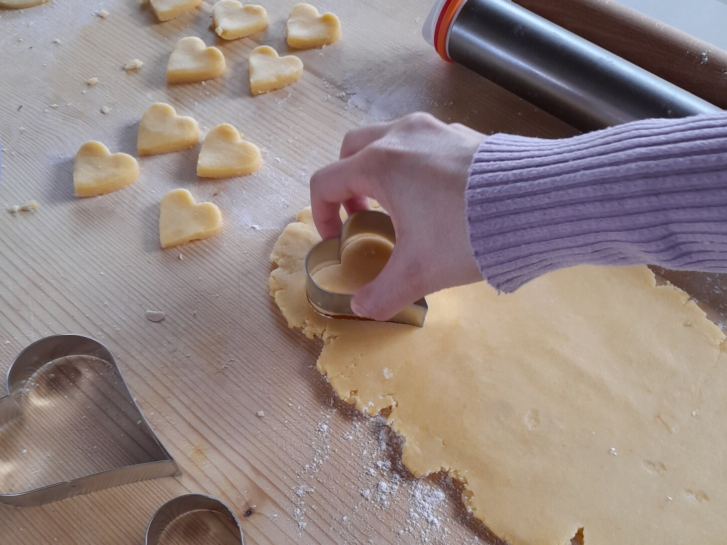 Una ragazza, di cui si vede solo la mano, sta premendo uno stampino a forma di cuore su un impasto steso per realizzare un biscotto.