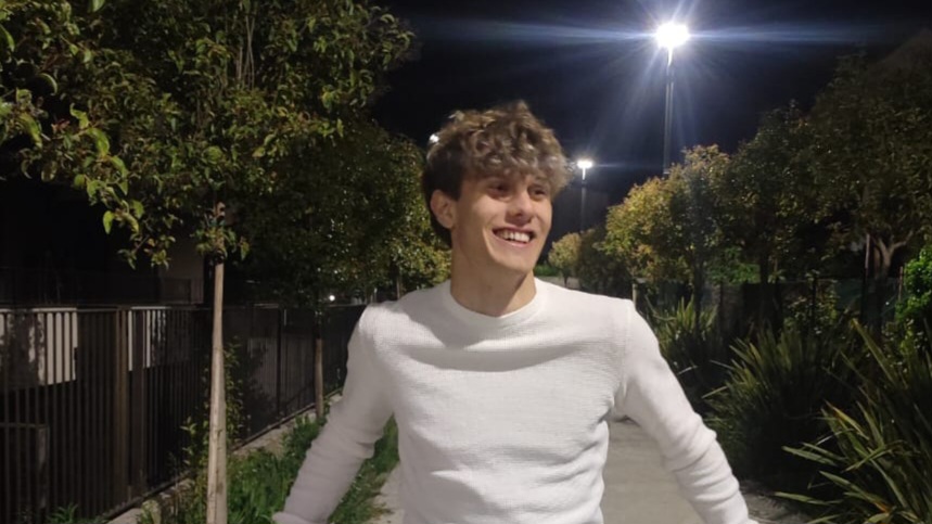 In questa foto Francesco ha i capelli ricci, un maglione chiaro e sorride. È sera
