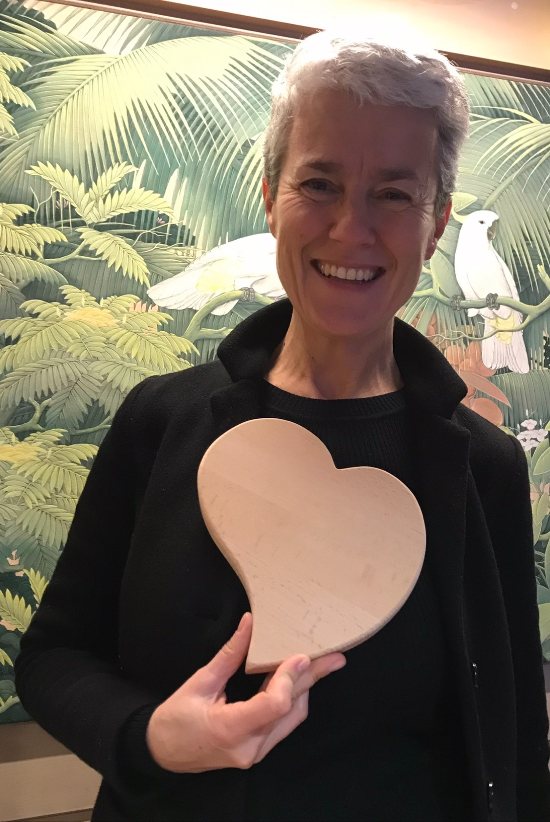 Federica sorride in questa foto. Tiene in mano un cuore di legno, ha i capelli corti e una maglia scura