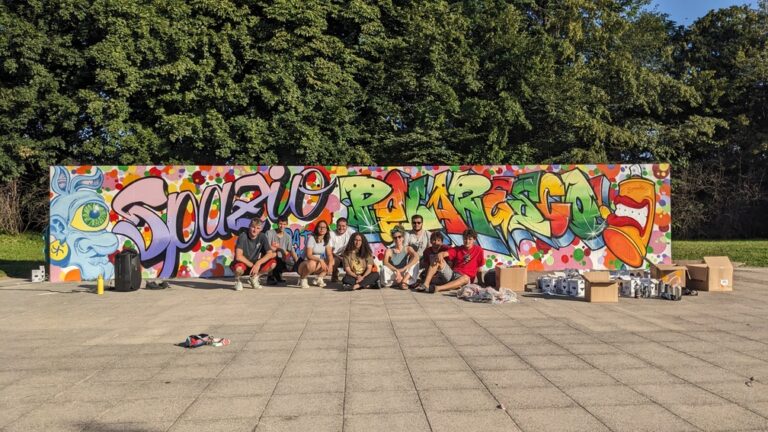 Un gruppo di giovani posa davanti a un murales che riporta la scritta 