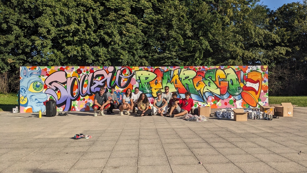 Un gruppo di giovani posa davanti a un murales che riporta la scritta 