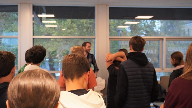 Un consulente di orientamento dialoga con il gruppo di studenti di spalle. Hanno abbigliamento sportivo.