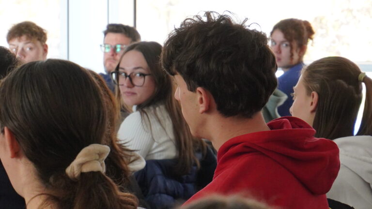 gruppo di studenti durante l'intervento di un consulente di orientamento dell'Informagiovani. Una persona con gli occhiali in secondo piano guarda in camera