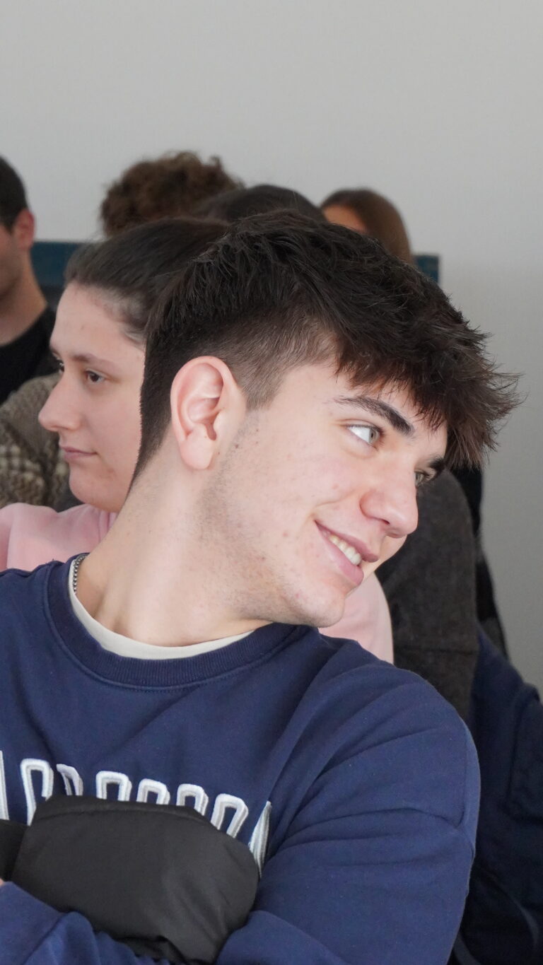 Primo piano di studente durante la giornata del placement. Ha una felpa blu, i capelli corti, gli occhi chiari e sorride.