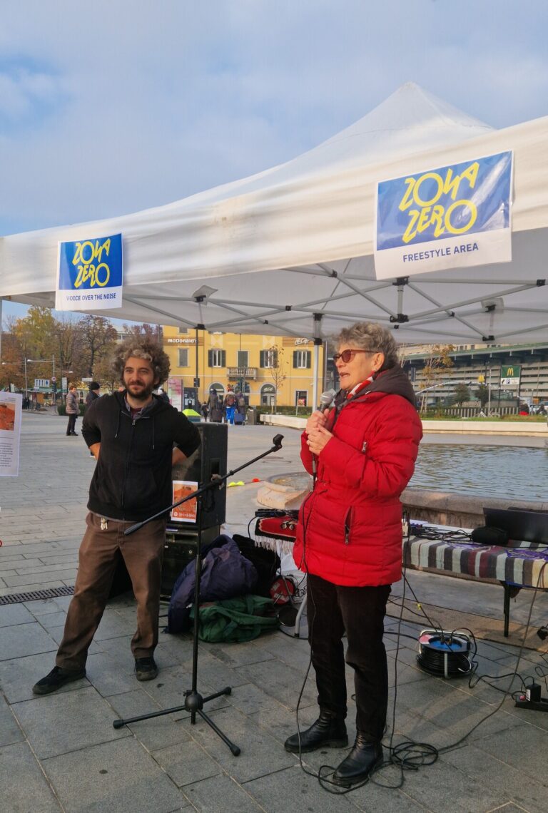 L'assessora alle Politiche per Giovani Marzia Marchesi è davanti a un gazebo allestito nel piazzale della stazione, insieme a un educatore di Giovani Onde. Sta parlando al microfono.