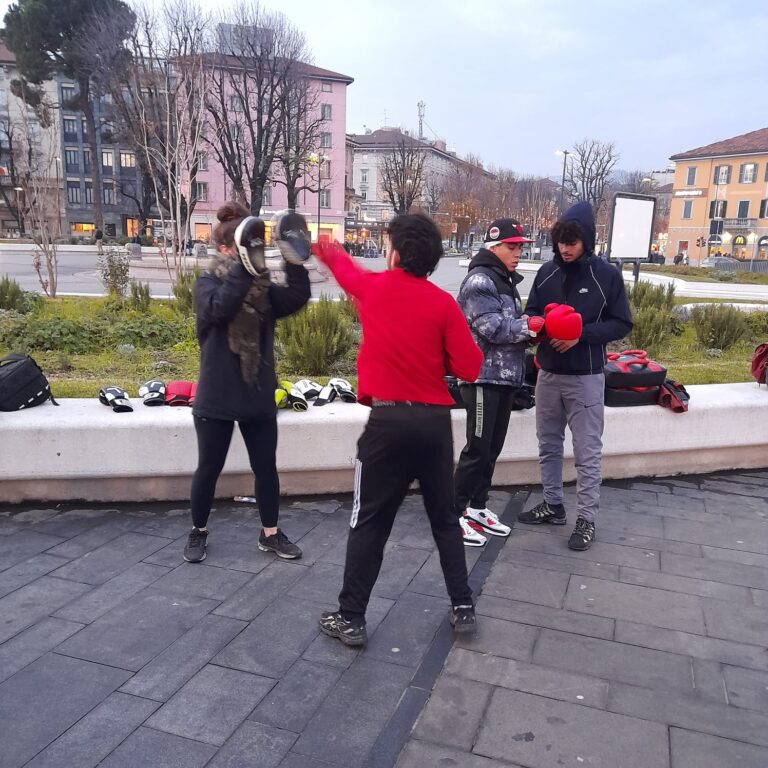 Tre ragazzi e una ragazza si allenano tirando di boxe nel piazzale della stazione.