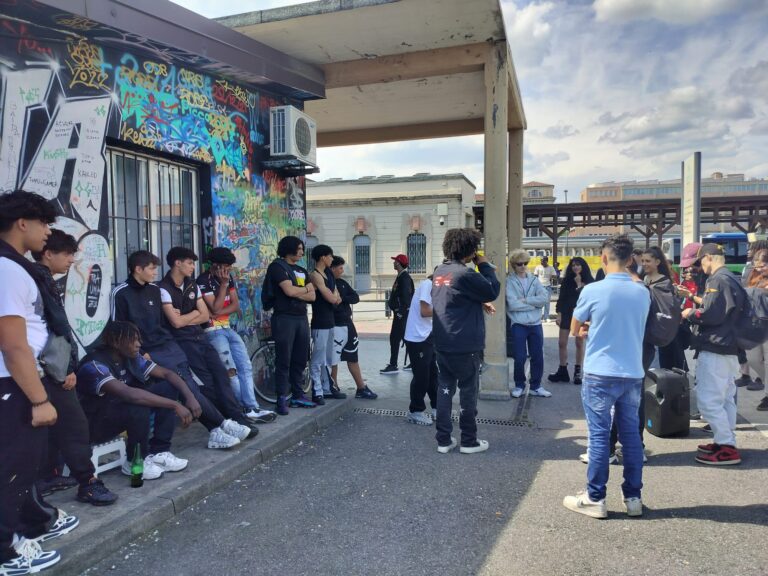 Un ragazzo fa free style davanti a Zona Zero, la fermata della TEB in stazione. Intorno a lui un gruppo numeroso di ragazze e ragazzi guarda e ascolta.
