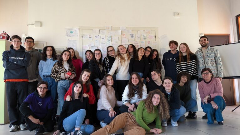 Un gruppo di studenti posa sorridente, guardando in camera. Alcune sono in piedi, altre sedute per terra davanti.