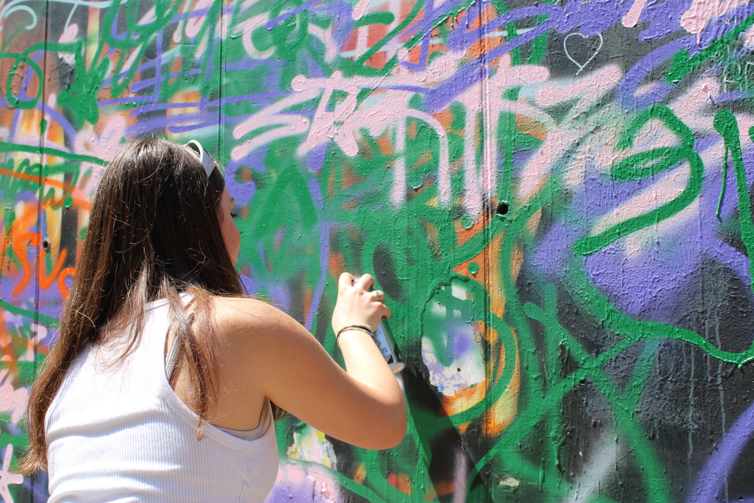 Una ragazza sta tracciando con una bomboletta spray delle scritte su un murales pieno di segni colorati indistinguibili.