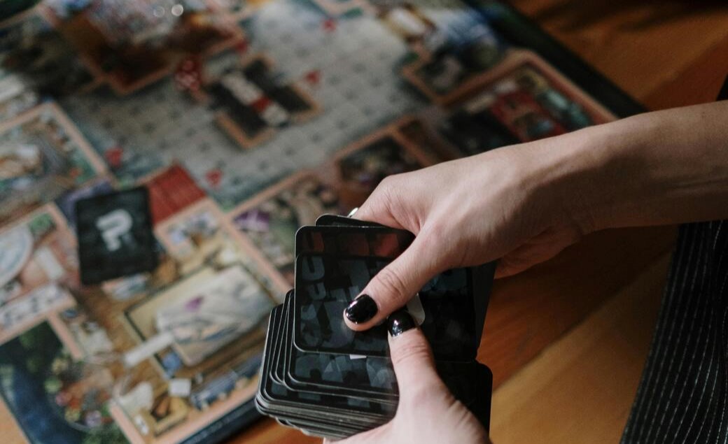 Immagine decorativa che ritrae il tabellone di un gioco da tavola. In primo piano delle piane mescolano delle carte da gioco.