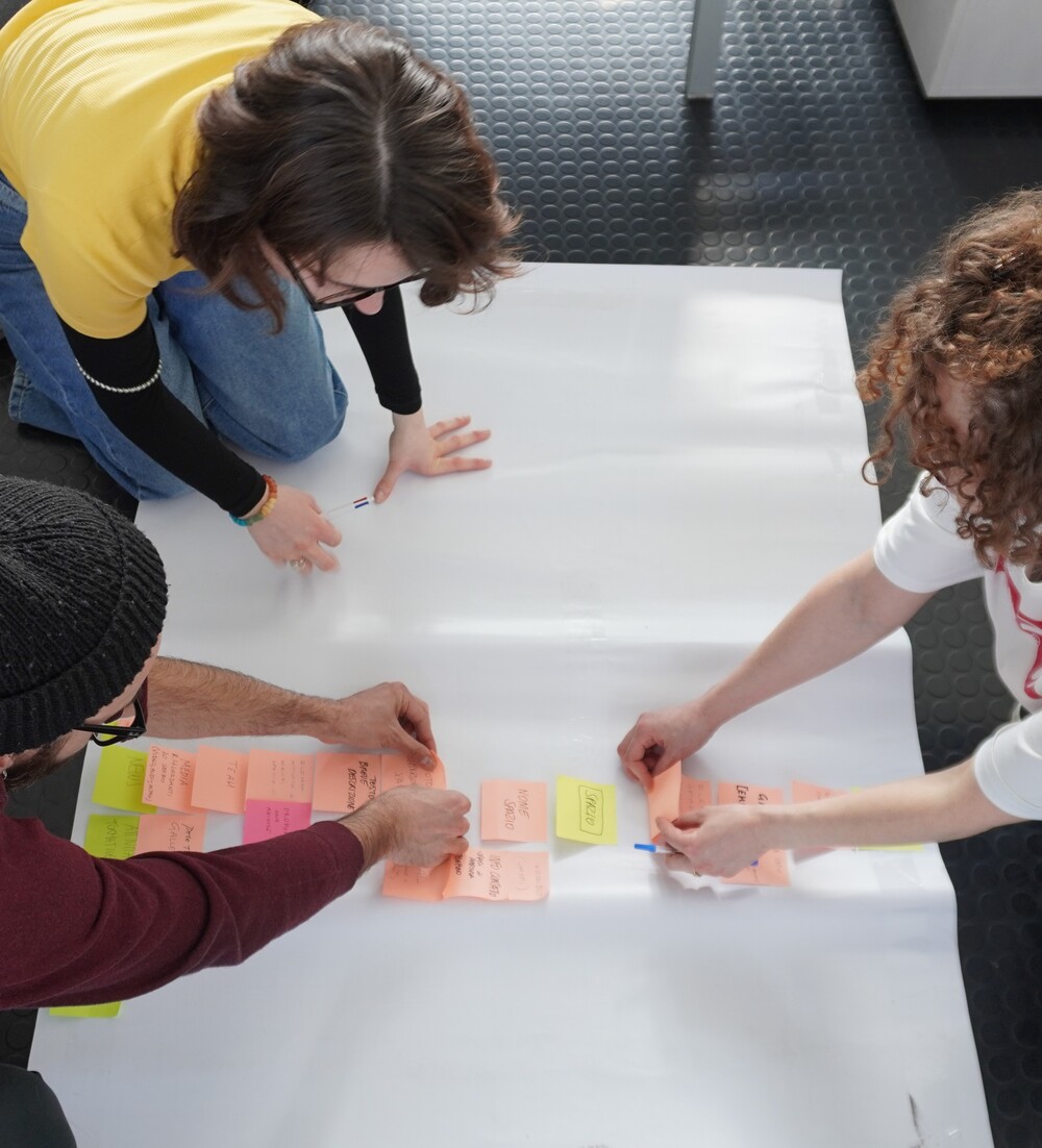 Tre persone, da sinistra un ragazzo e due ragazze, stanno ordinando dei post-it su un cartellone bianco per rappresentare la struttura del sito di Bergamo per Giovani.
