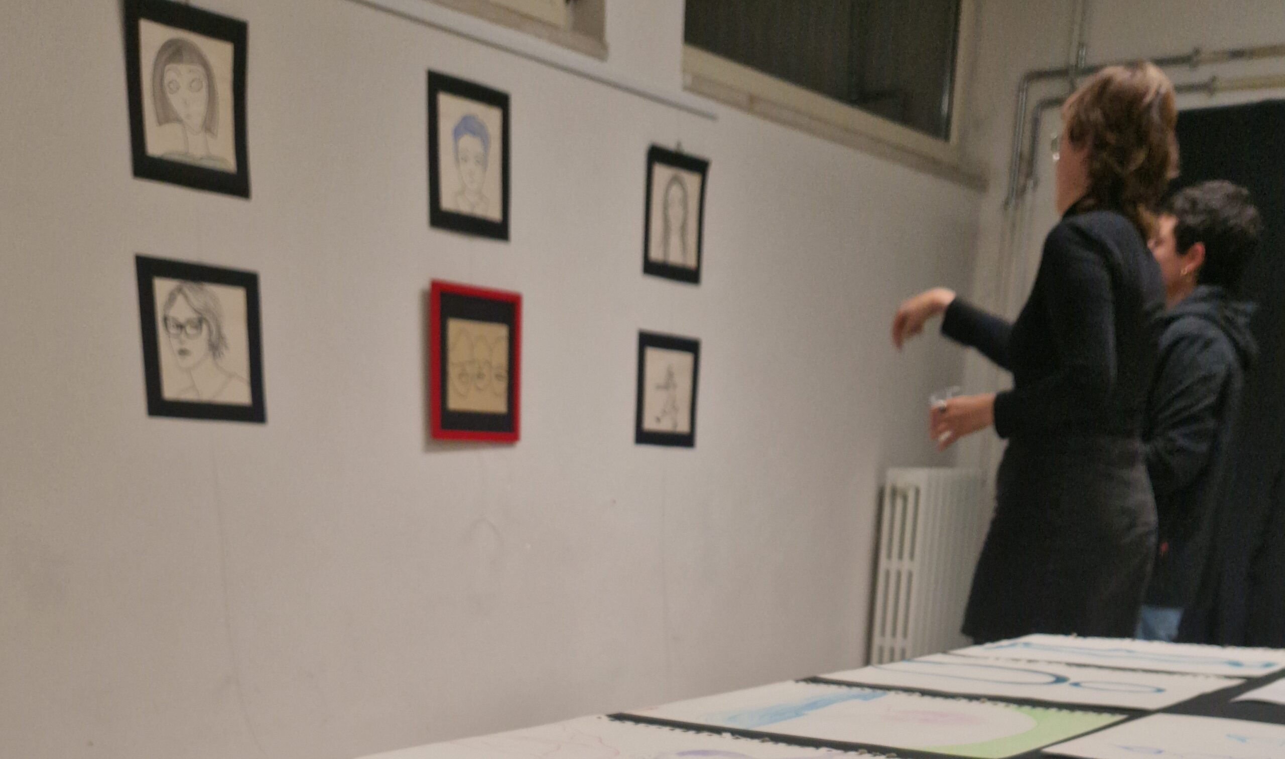 Due ragazze stanno osservando dei disegni esposti lungo una parete.