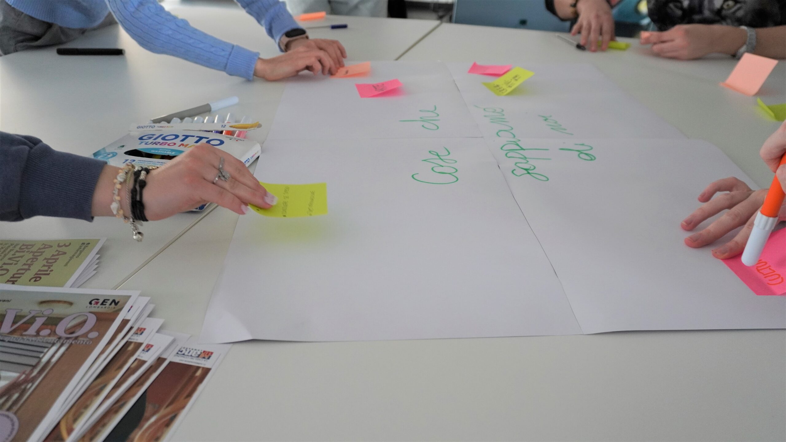 Diverse mani che scrivono su un cartellone e attaccano dei post-it. Sul cartellone c'è scritto: Cose che sappiamo di noi