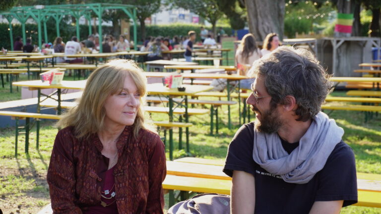 Cristina e Giorgio dell'Informagiovani sorridono mentre si parlano. Siedono su una panchina nel parco di Edoné