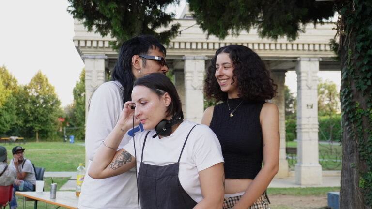 Tre giovani in uno spazio aperto. Una persona del gruppo sta suonando da DJ