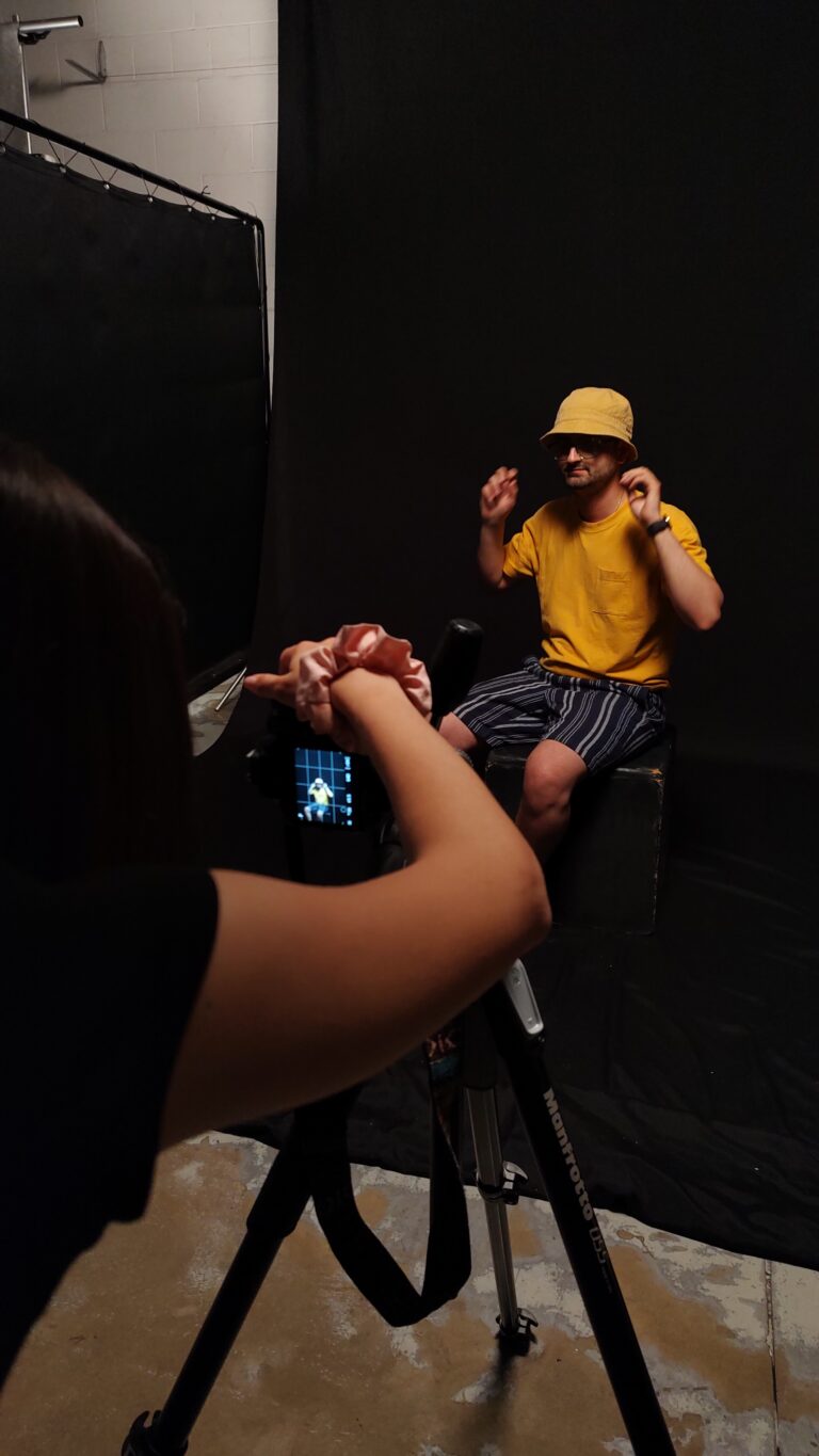 immagine di backstage: si vede un braccio che reoìgola una macchina fotografica e una persona ritratta su sfondo scuro.