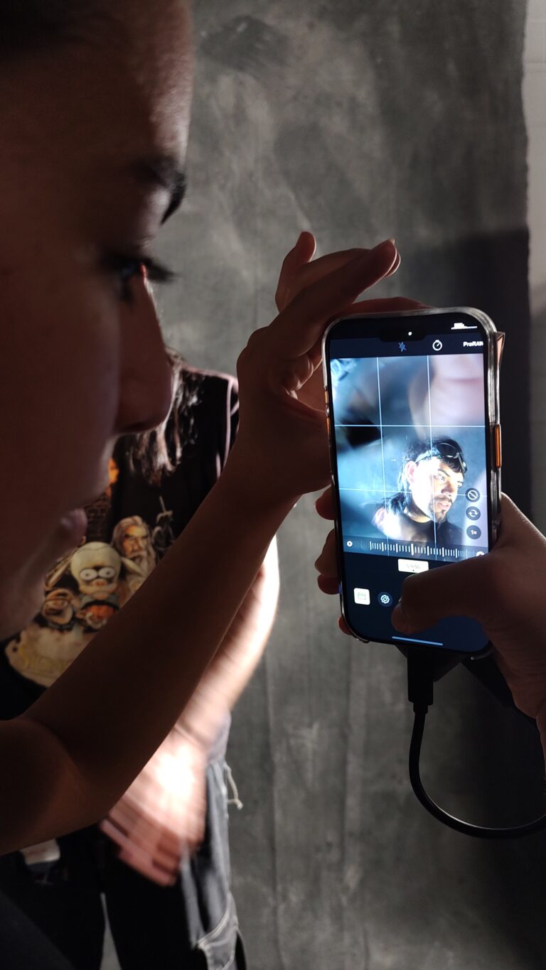Immagine che ritrae in primissimo piano il profilo di una persona che scatta una foto su uno smartphone. Sullo schermo dello smartphone si vede la persona che sta per essere fotografata con effetti di luce sul volto.