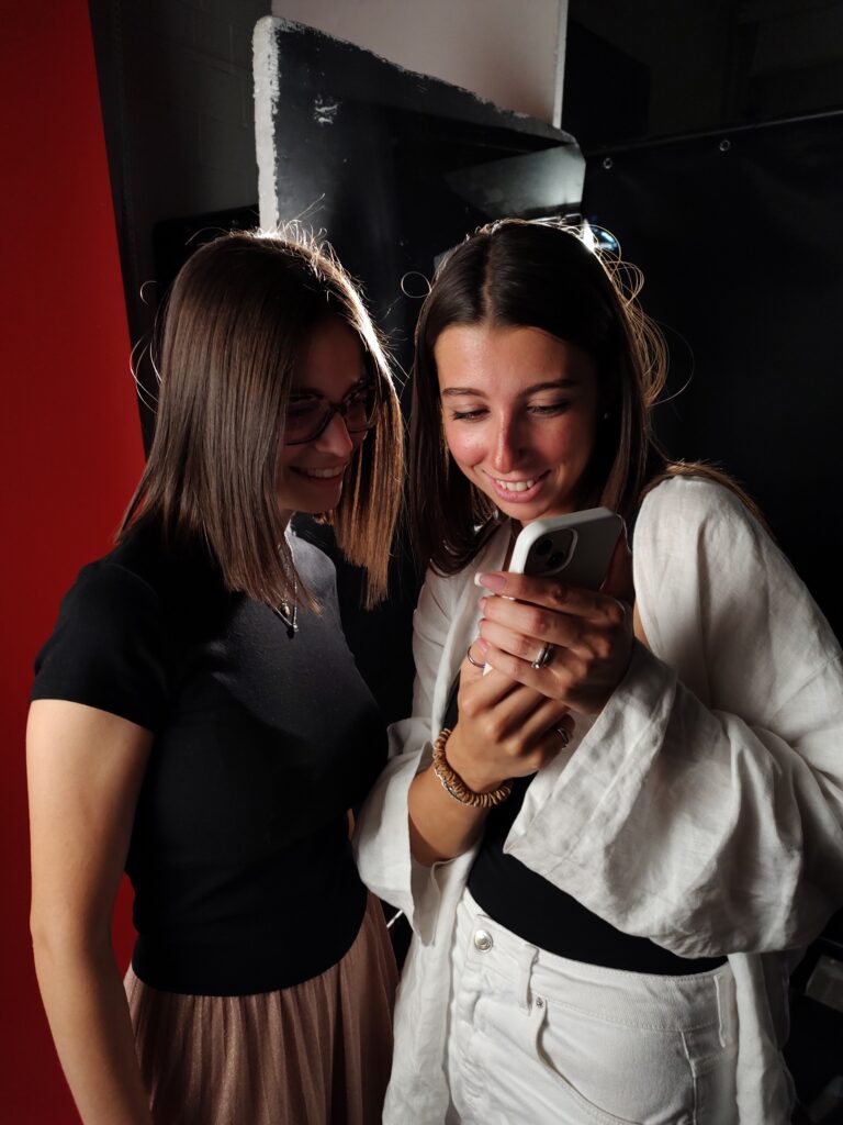 Due persone in uno studio fotografico guardano alcuni scatti sul telefono e sorridono.