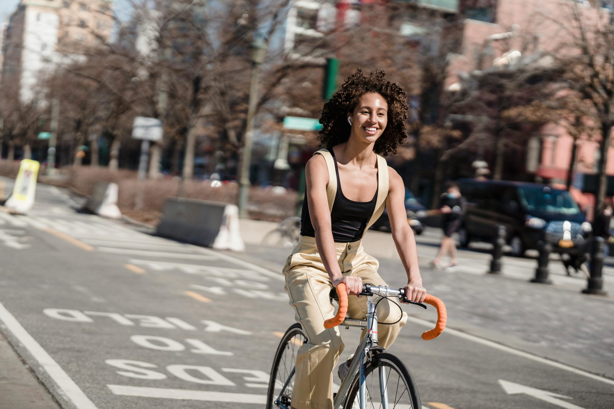 giovane che gira per la città in bici, sorride, ha i capelli ricci e scuri, una maglietta scura e pantaloni chiari.