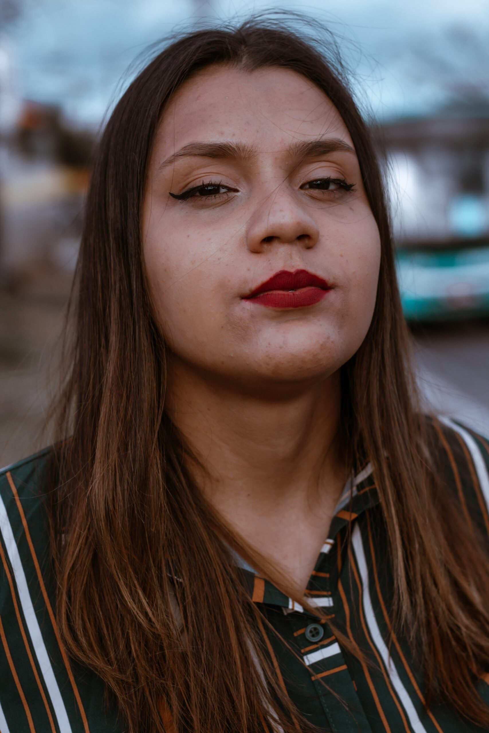 Primo piano di una ragazza con i capelli lunghi e castani e una camicia scura a righe colorate.