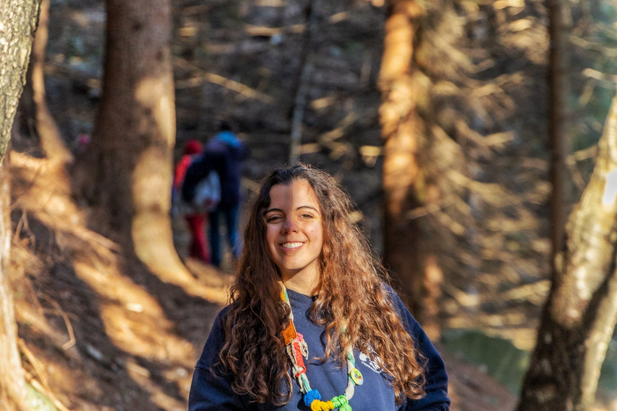 Anna in piedi nel bosco, indossa una felpa blu e porta il fazzolettone scout al collo.