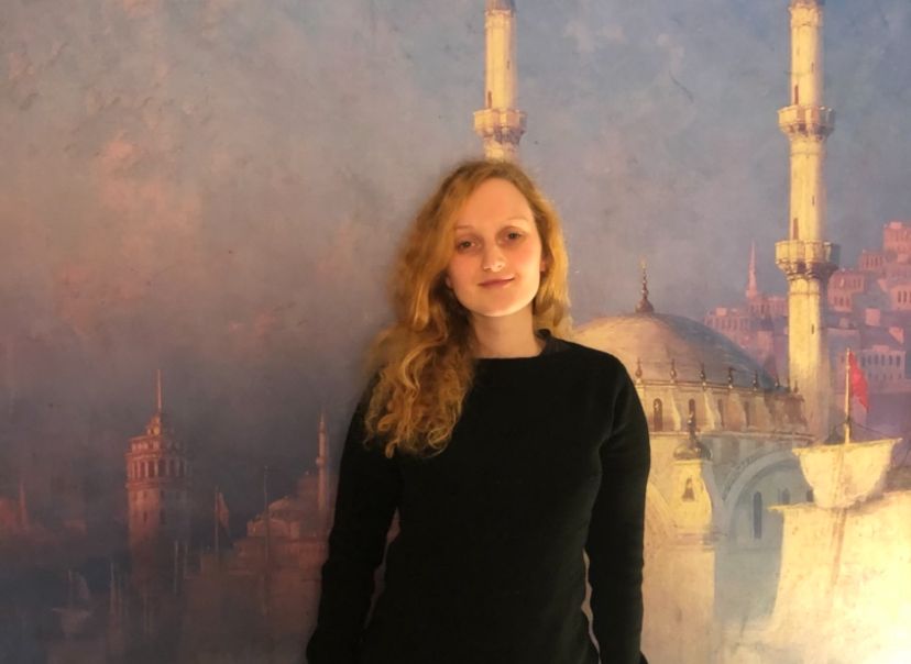 Giulietta di fronte all'immagine di una città, ha una maglia scura, i capelli ricci e chiari.