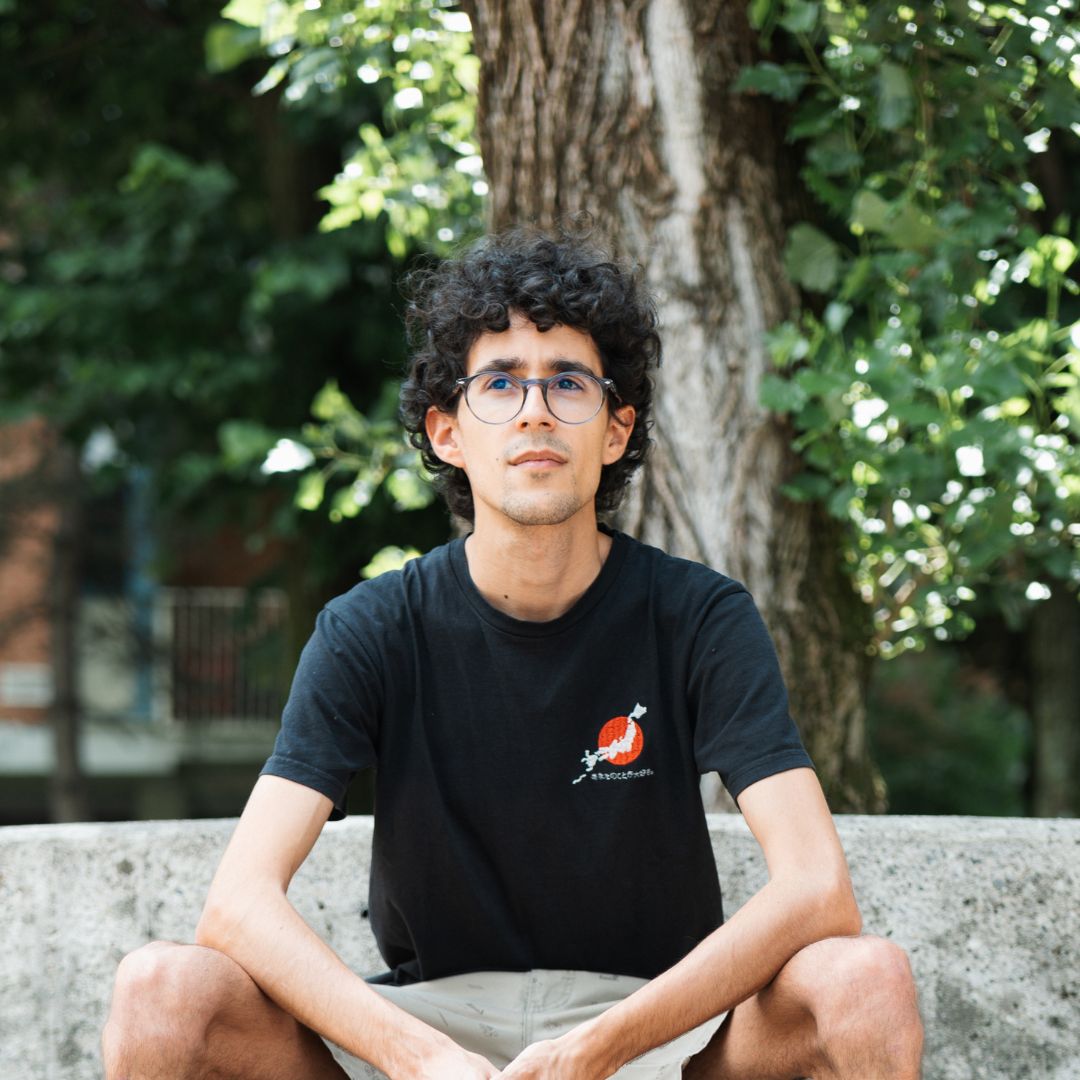 Luca è in posa, circondato da alberi. Guarda in camera, ha una maglia scura.