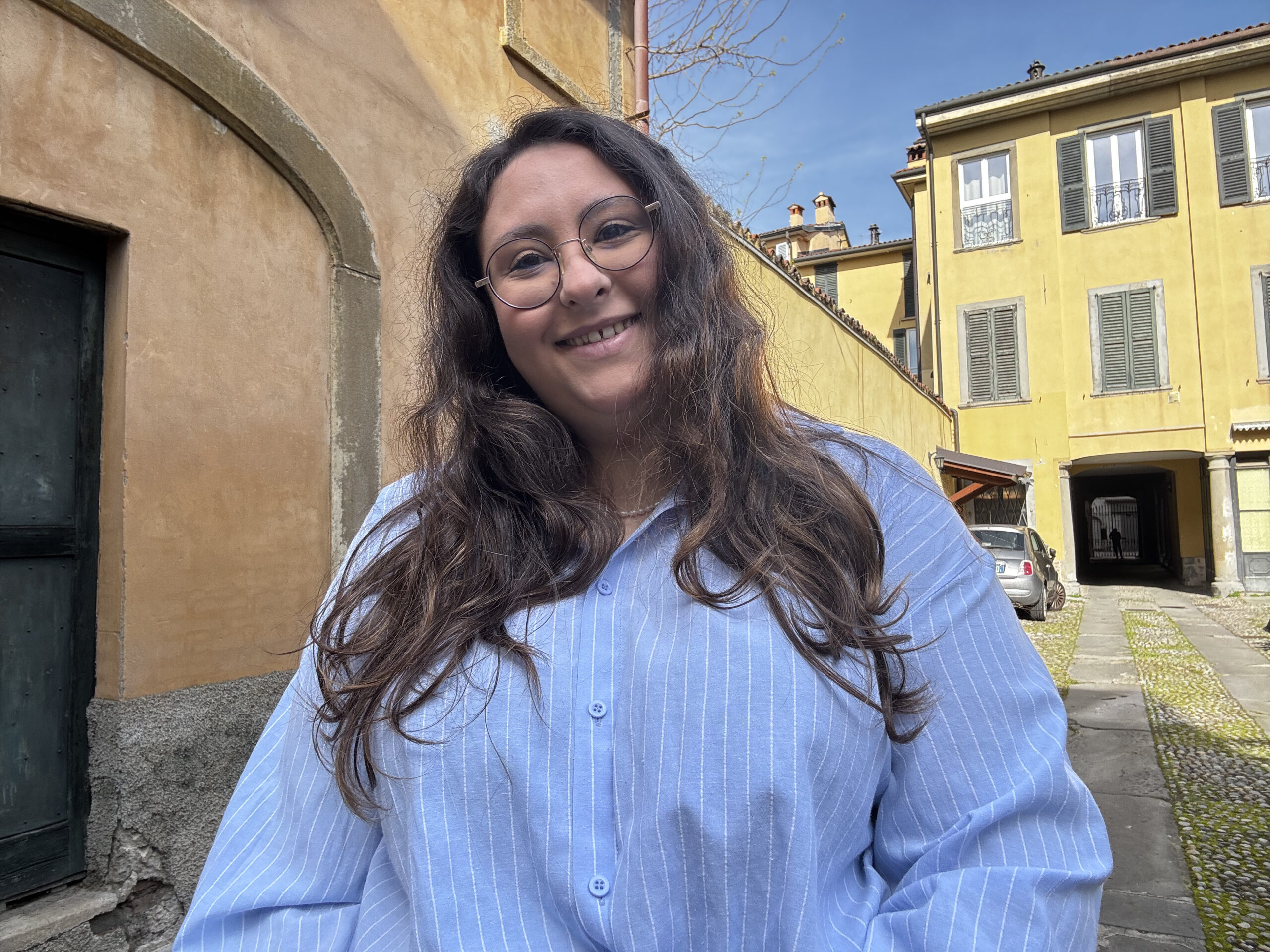 Lucrezia sorridente, indossa una camicia azzurra. Sullo sfondo si vedono degli edifici