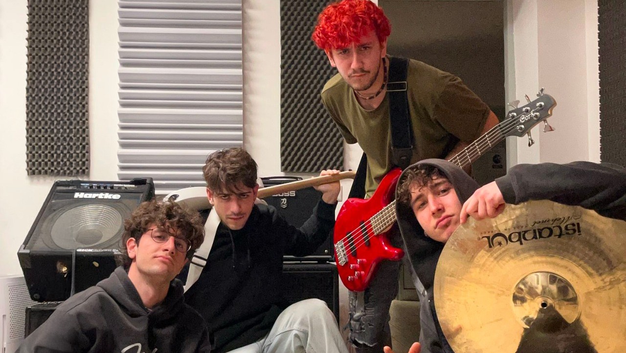 Quattro ragazzi posano con i loro strumenti musicali dentro una sala prove