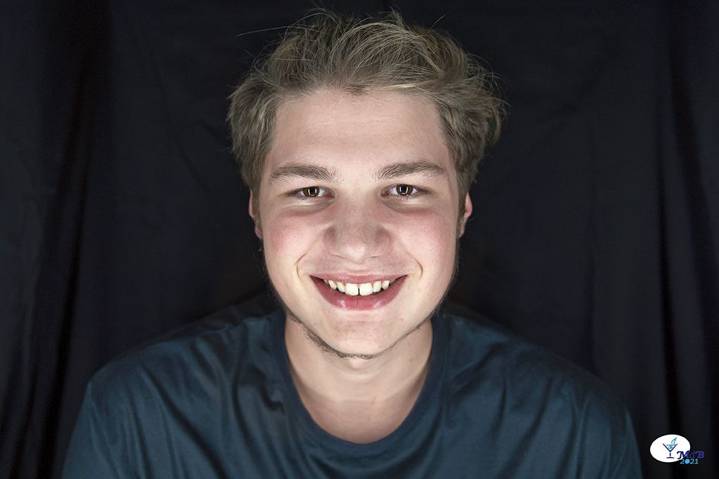 Primo piano di Tommaso. Nella foto sorride, indossa una maglietta grigio scura. Ha i capelli biondi e corti.
