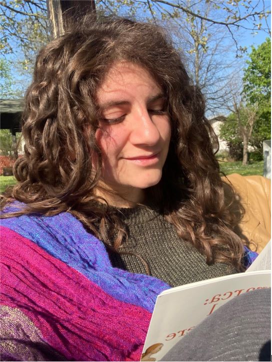 Giorgia legge un libro, indossa una maglia grigia e una sciarpa colorata