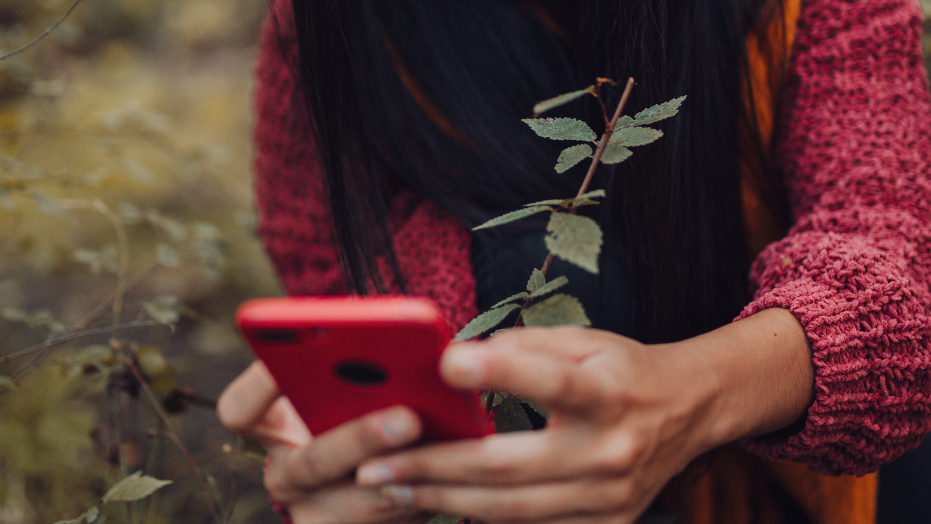 Primo piano di una ragazza in un contesto naturale boscoso che fotografa con uno smartphone qualcosa che rimane fuori dall'inquadratura