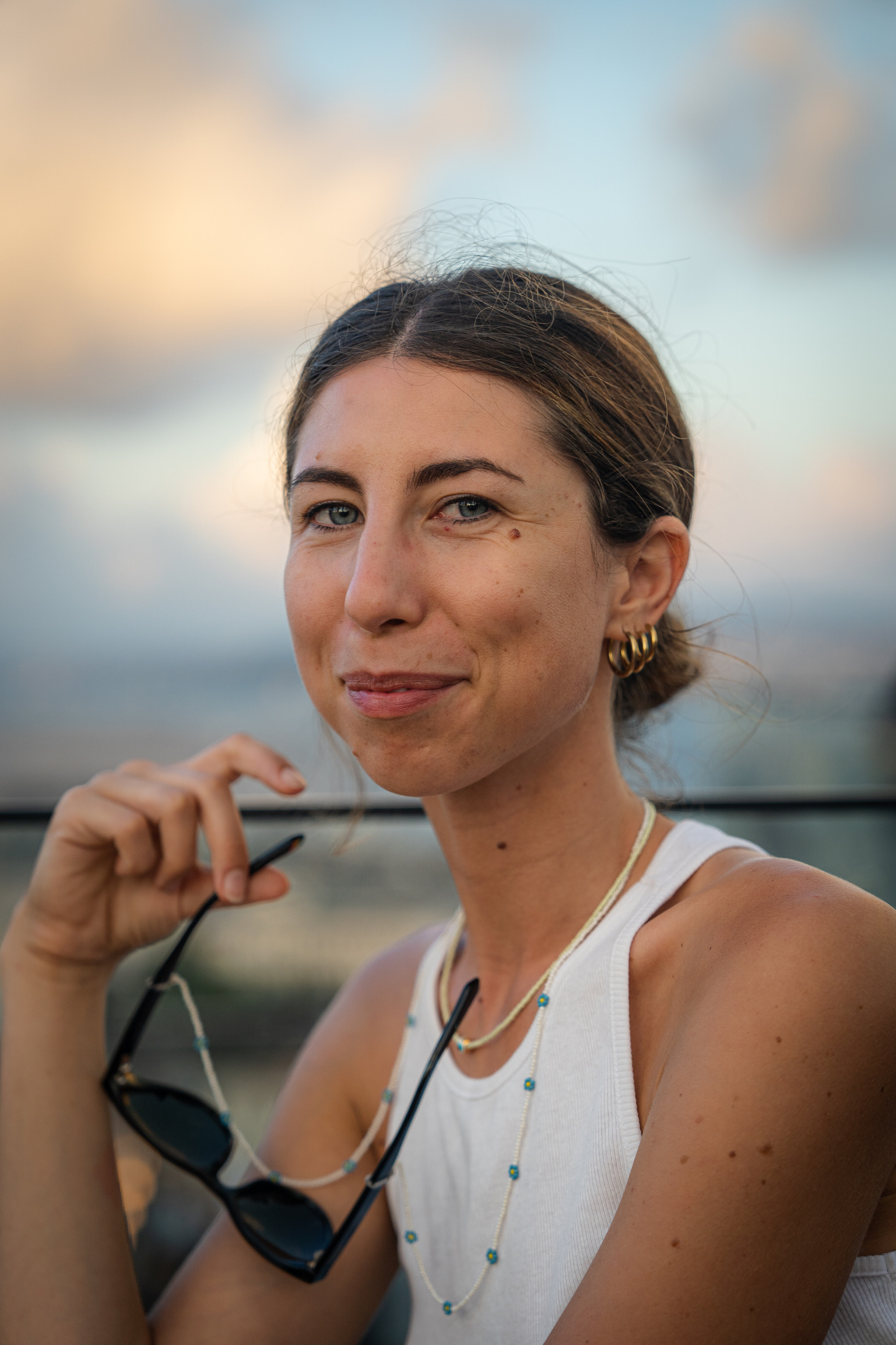 Primo piano di Simona. Sulla sfondo il cielo serale, tiene in mano gli occhiali da sole.