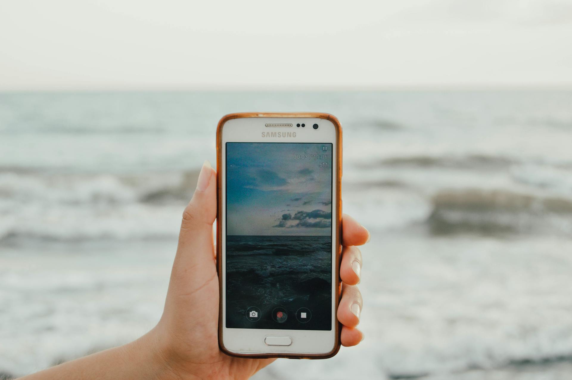 immagine di una mano che regge un telefono che filma il mare