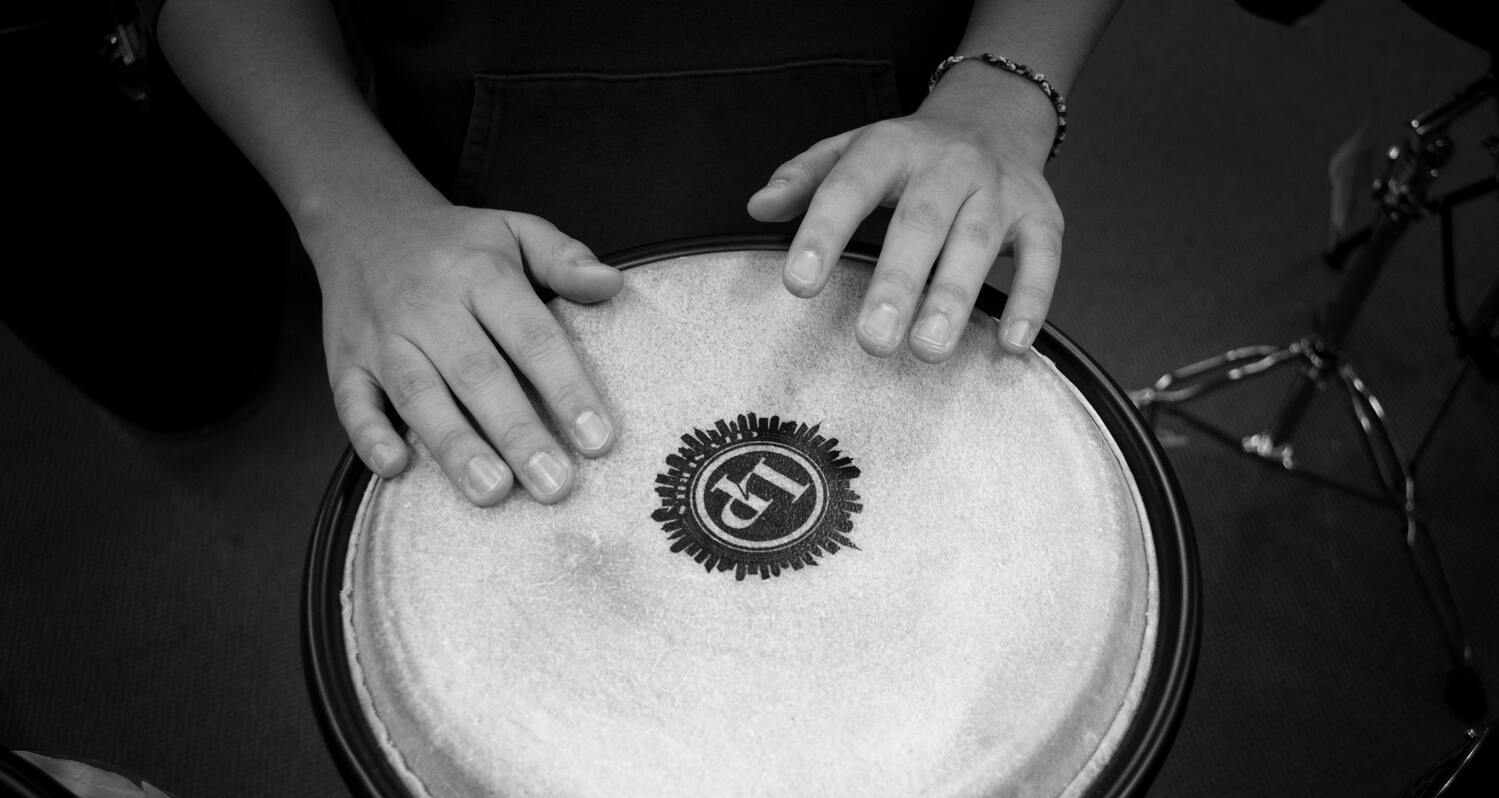 Primo piano di due mani che suonano uno strumento a percussione. La foto è in bianco e nero.