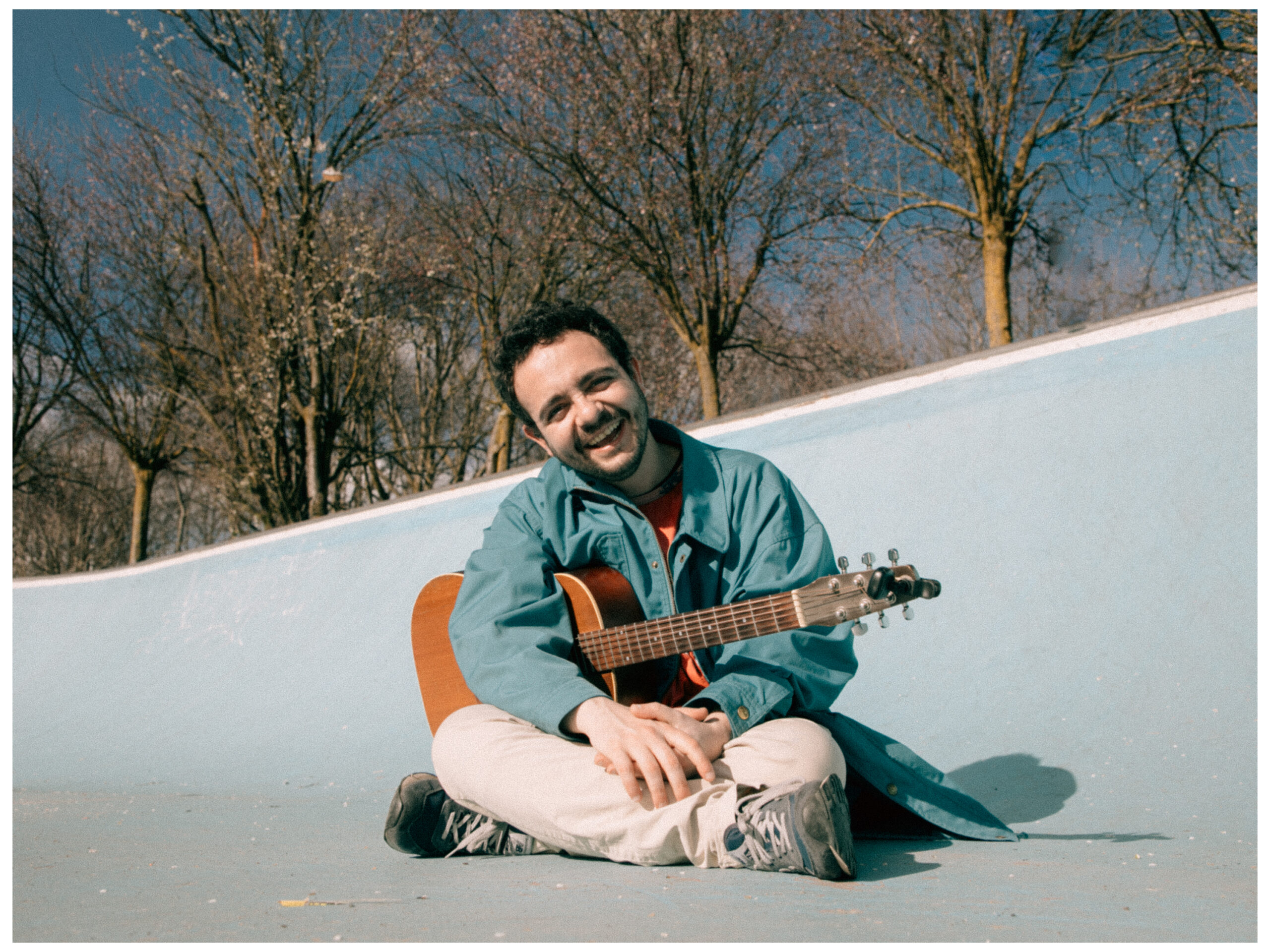 Giulio è seduto a gambe incrociate sul pavimento e imbraccia la sua chitarra