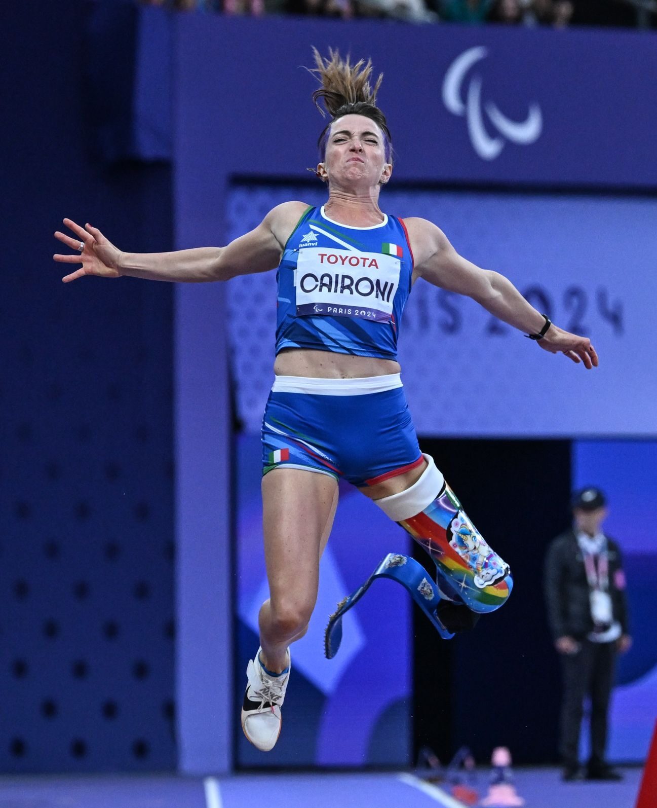 Martina Caironi durante una gara, salta. Indossa dei calzoncini azzurri e una canottiera con scritto sopra il suo cognome.