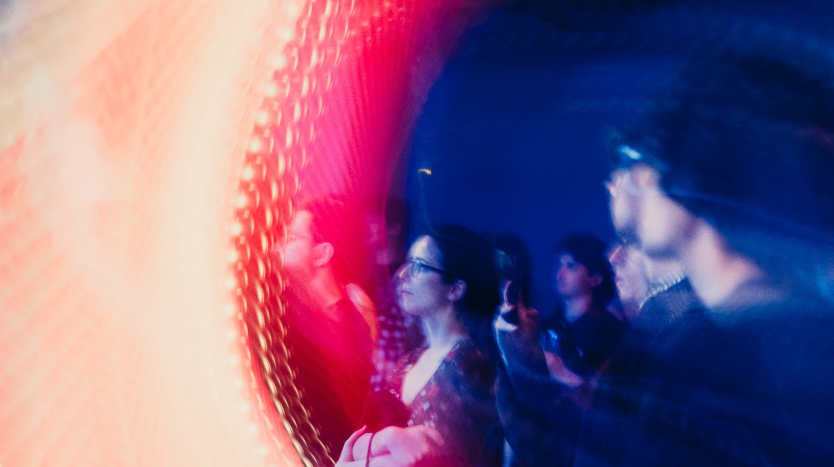 Nella parte destra della foto un gruppo di ragazzi e ragazze guarda nella stessa direzioni. L'ambientazione è notturna, con una luce blu che trasfigura i colori naturali. Nella parte sinistra della foto una un fascio di luce molto deciso, tra il giallo e il rosso, creato volutamente con la sovraesposizione, dà un effetto dinamico alla fotografia, coprendo i soggetti.