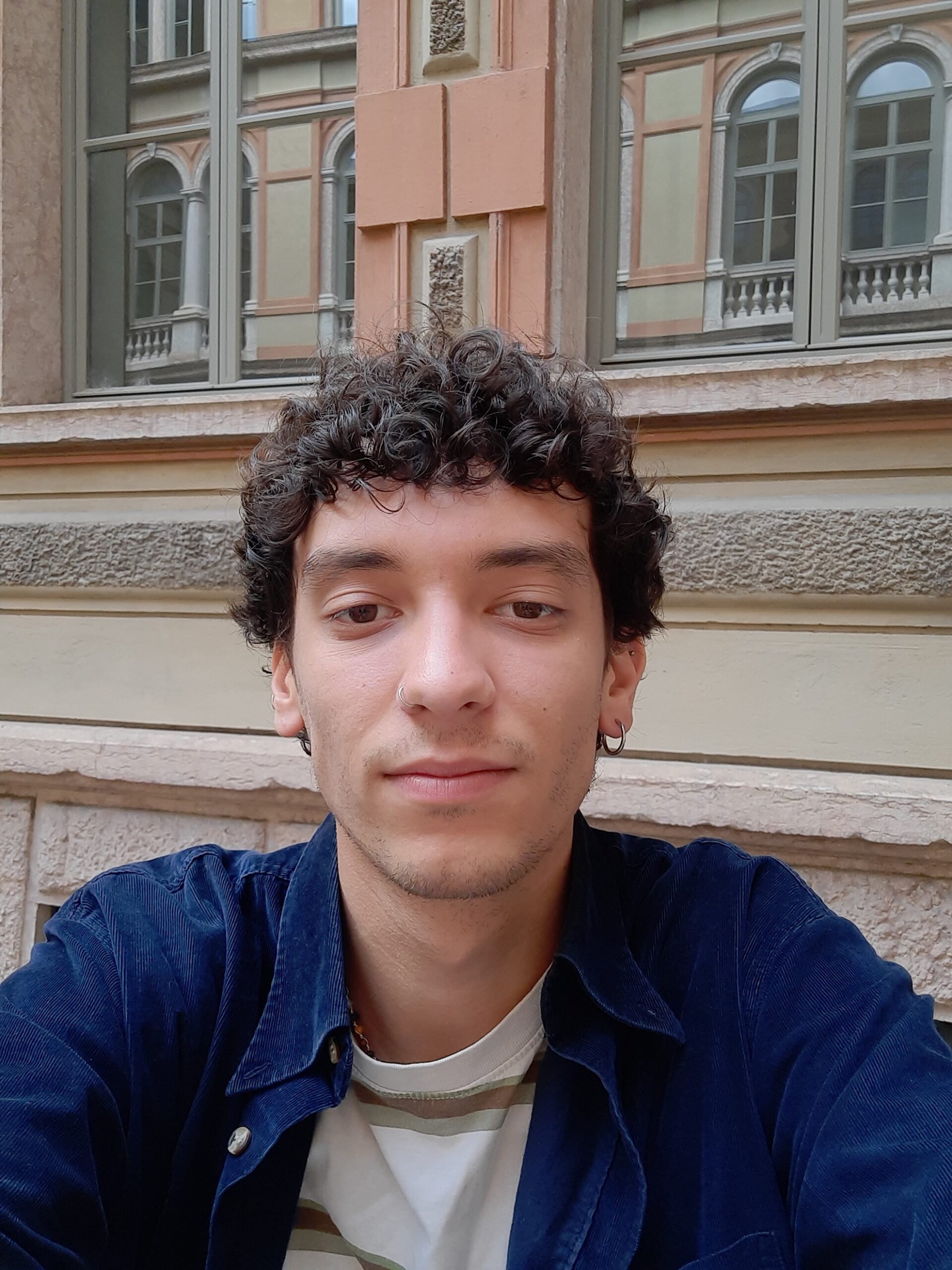 Primo piano di Matteo di fronte ad una finestra, indossa una giacca blu e una maglietta bianca.