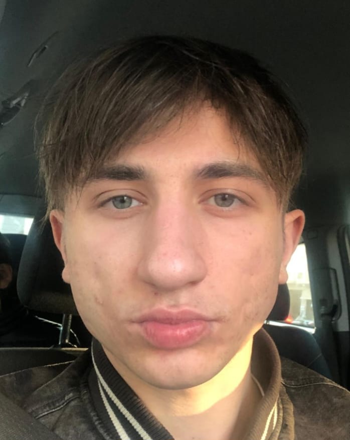 Davide che è seduto in una macchina, ha i capelli corti e scuri, indossa una giacca.