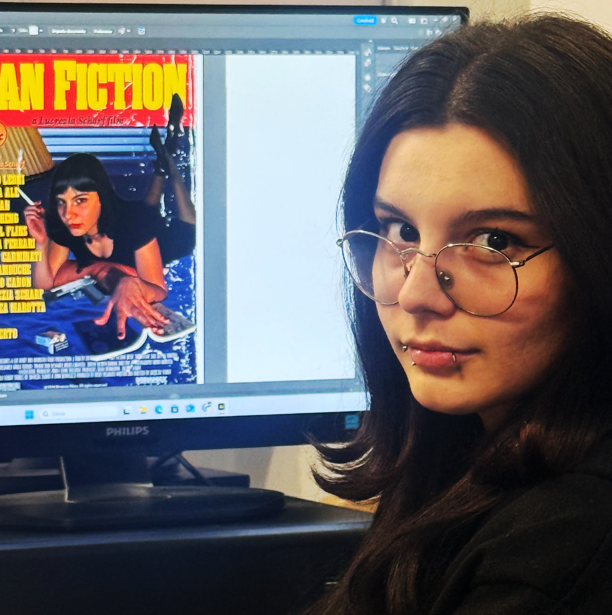 Lucrezia è seduta, dietro di lei c'è un computer e aperto un lavoro di grafico con la copertina di pulp fiction. Porta gli occhiali, ha i capelli lunghi e scuri.