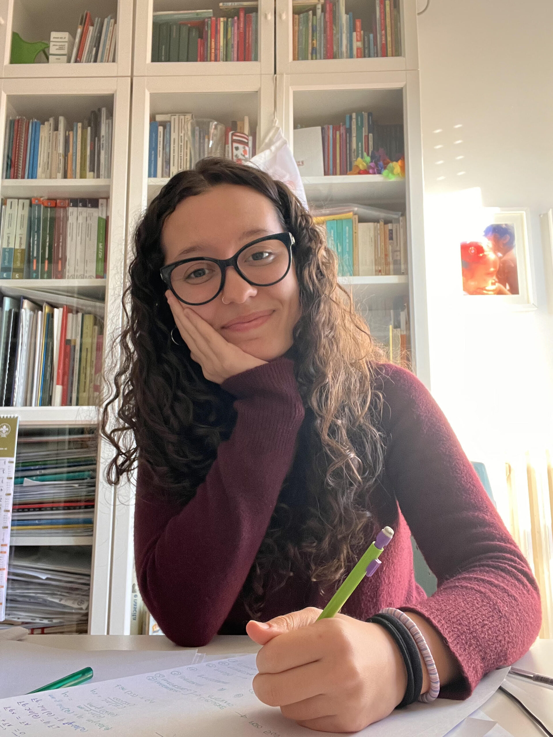 Sofia in una foto seduta. Sorride, tiene il volto appoggiato su una mano, nell'altra una matita. Dietro di lei una libreria. Ha un maglione bordeaux