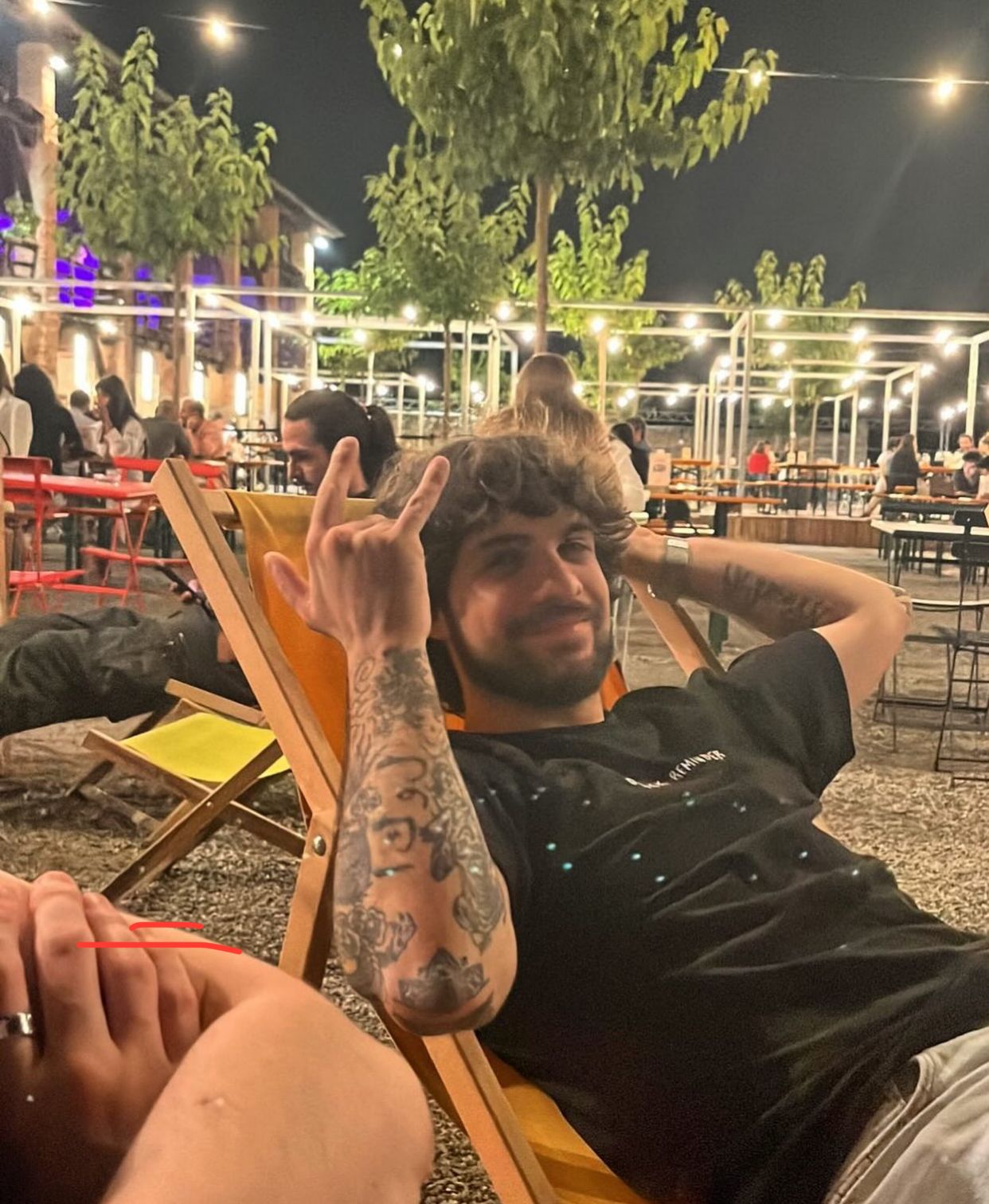 Nicola che è seduto su una sdraio in un locale all'aperto con delle lucine, ha i capelli scuri e indossa una maglietta nera.